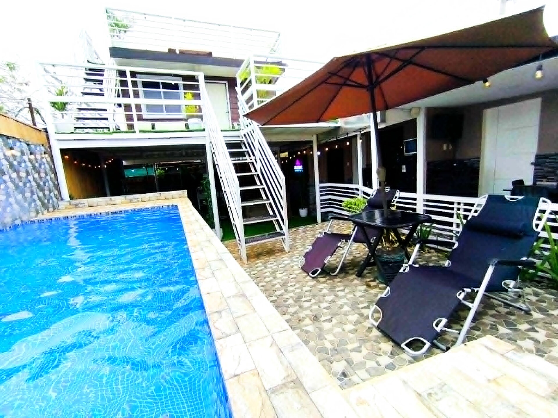 Private pool with poolside lounge chairs and orange umbrella by the day