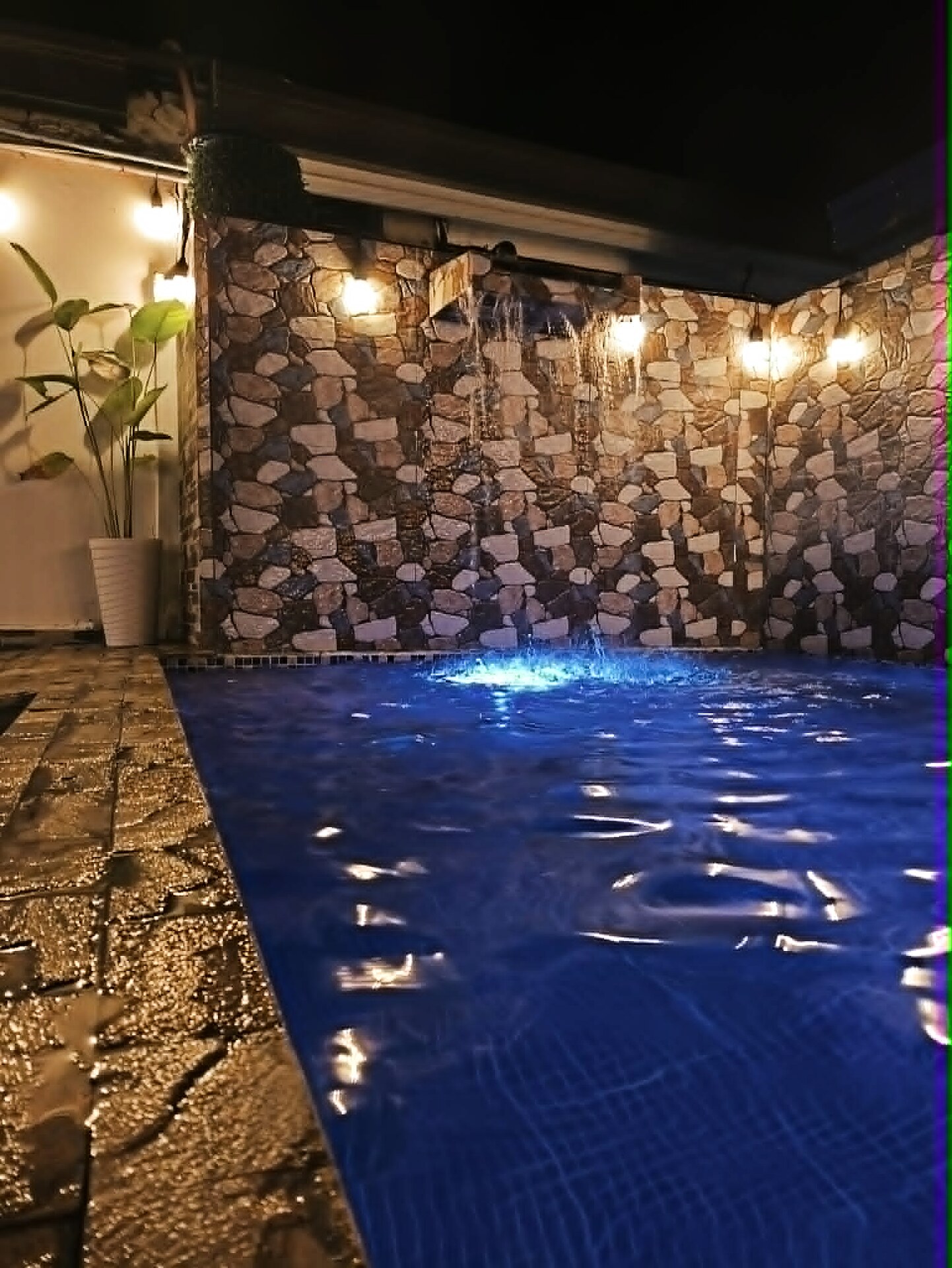 Pool with stone wall waterfall feature illuminated at night